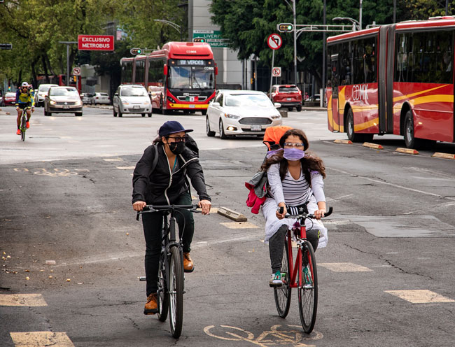 Personas en bicicleta entre automóviles y autobuses en una avenida